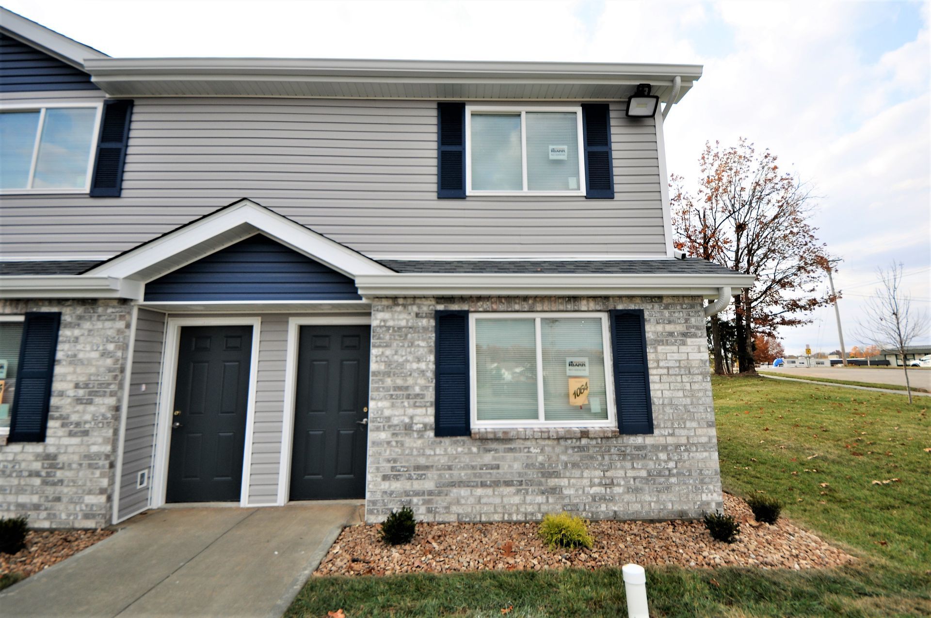 Two-story townhouse with gray siding, brick lower facade, and a front walkway.