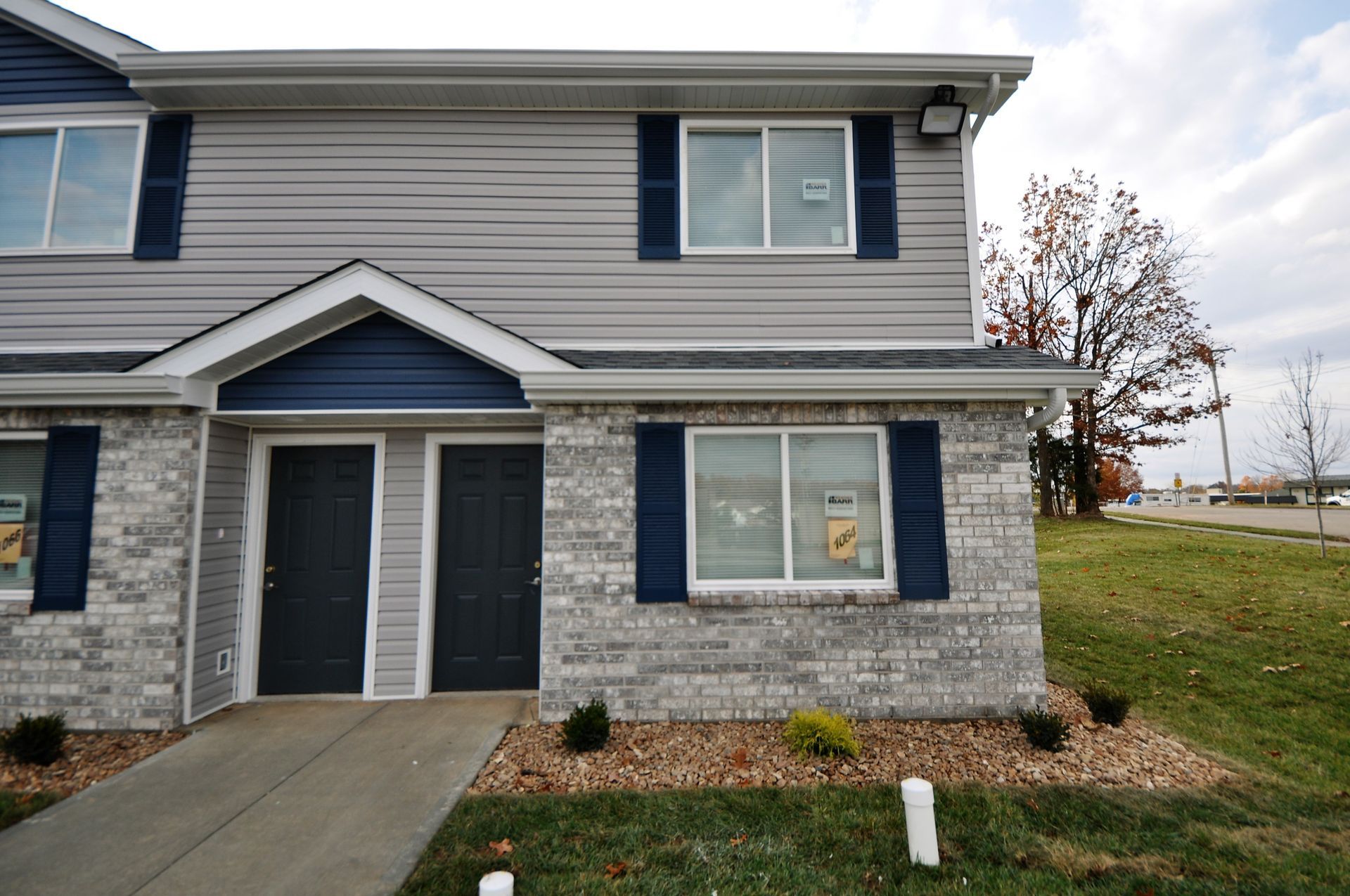 Two-story townhouse with gray siding, blue shutters, and a small front porch by a grassy lawn