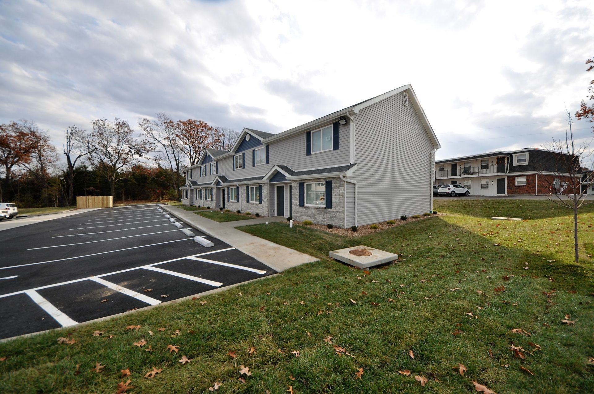 Row of gray townhouses beside a striped parking lot and grassy lawn on a cloudy day