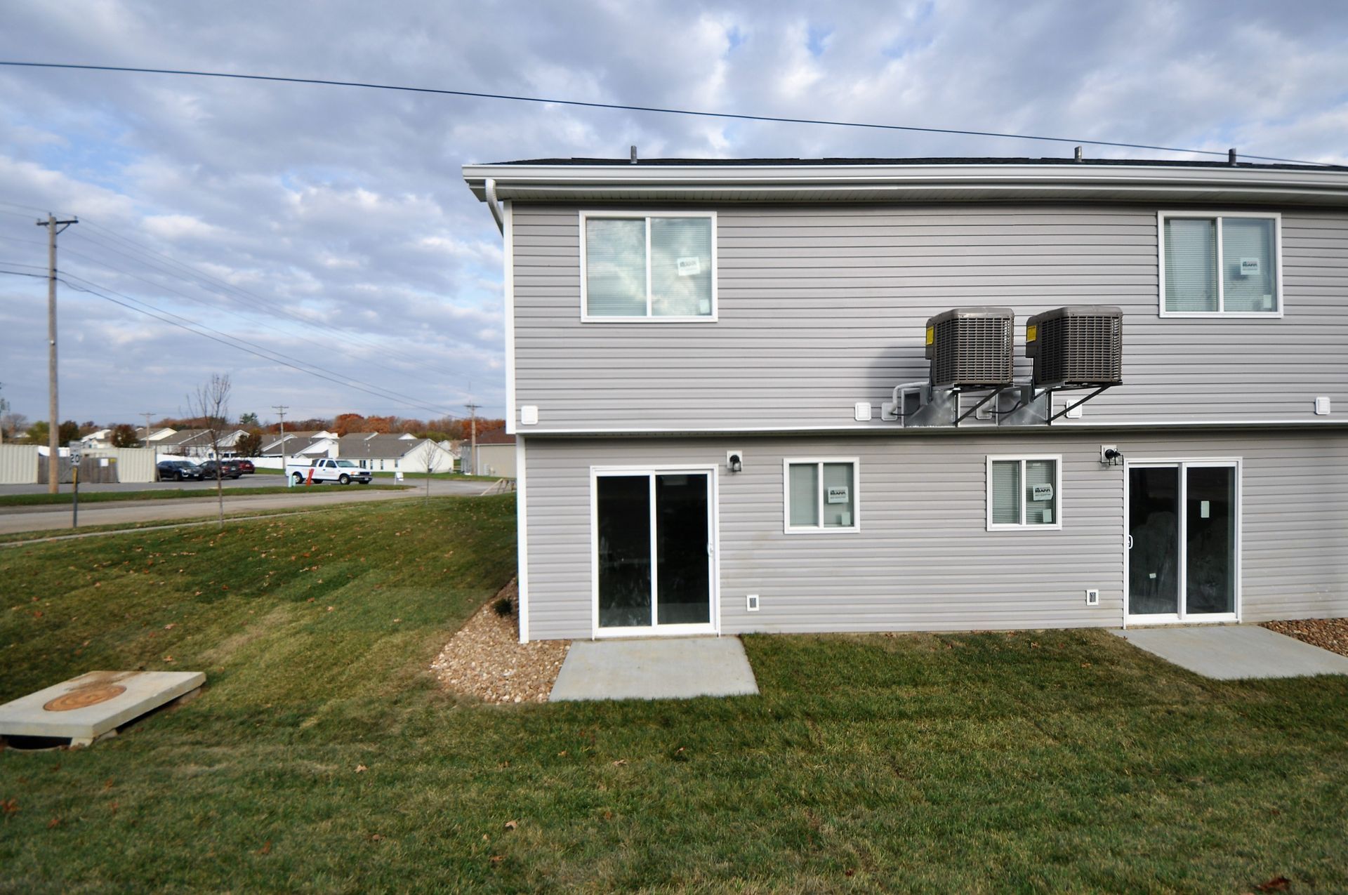Apartment building exterior with gray siding, sliding glass doors, and grassy lawn beside a street