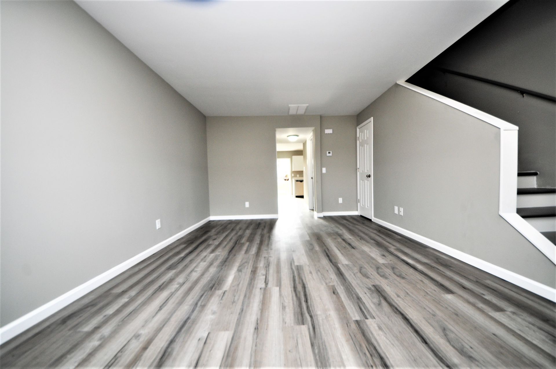 Empty modern living room with gray walls, wood-look floors, and a staircase on the right