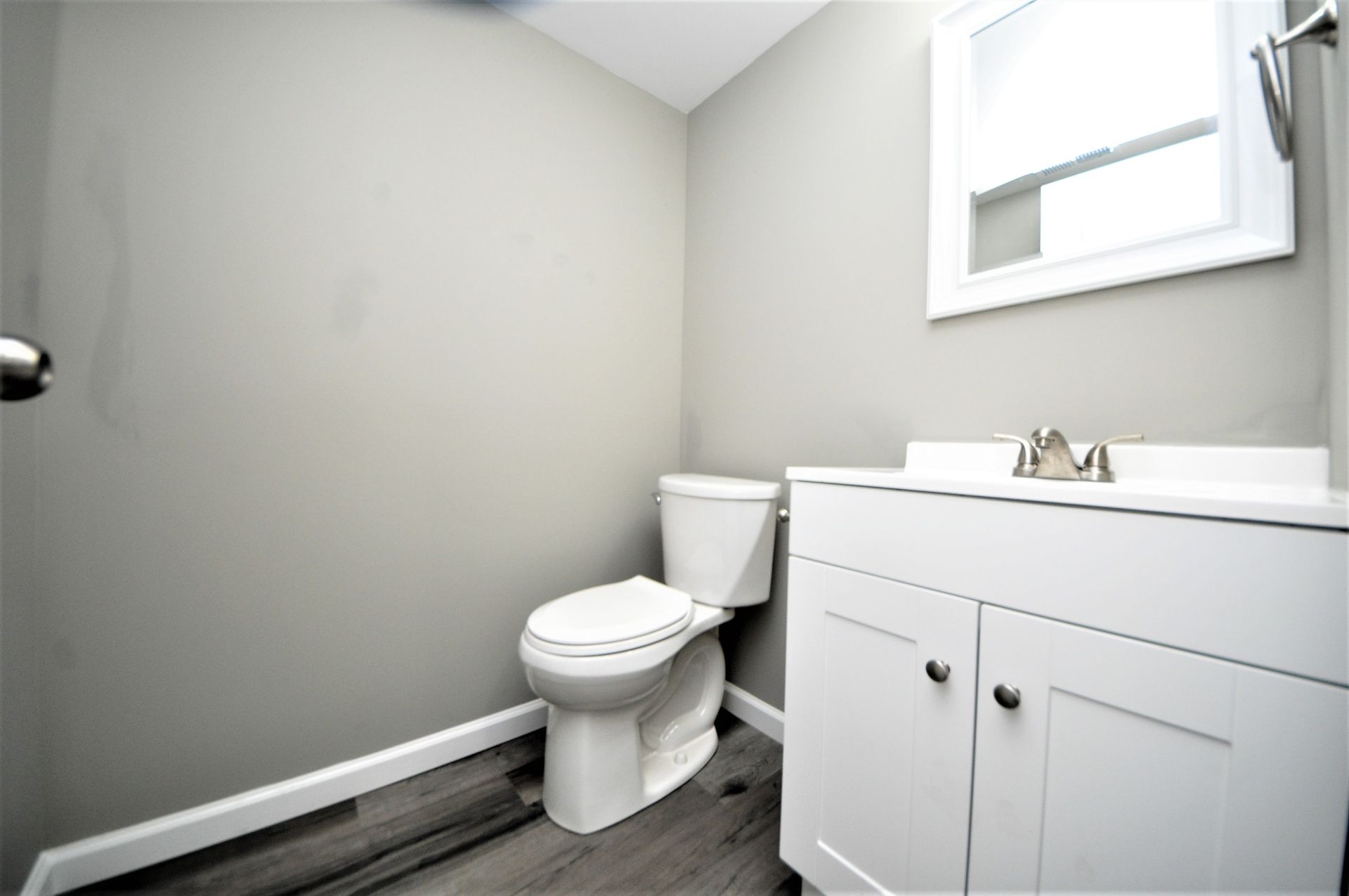 Small bathroom with toilet, white vanity, and window on gray walls