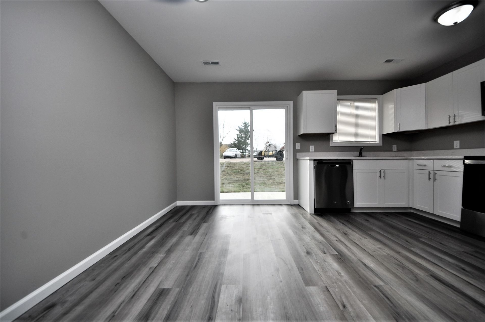 Empty modern kitchen with gray walls, wood-look flooring, white cabinets, and sliding glass doors.