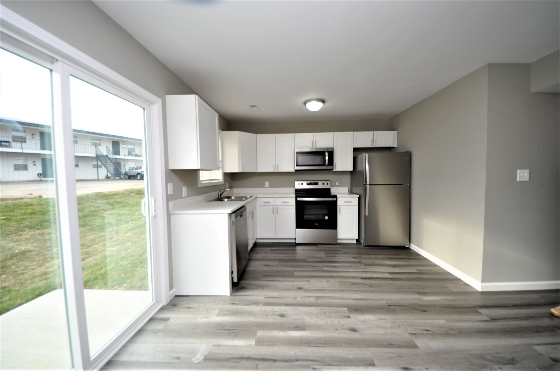 Empty modern kitchen with white cabinets, stainless steel appliances, and sliding glass door to a lawn
