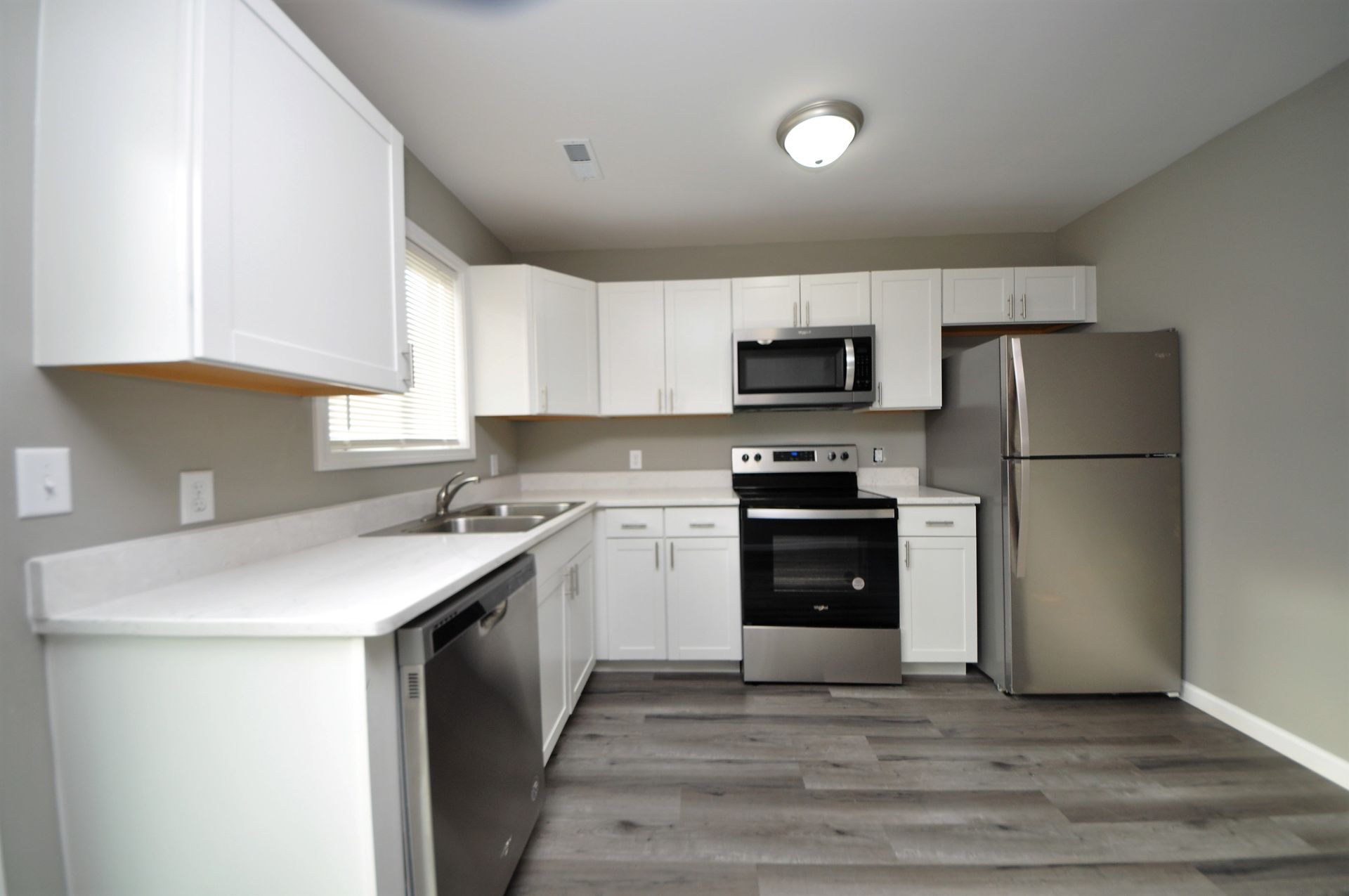 Modern white kitchen with stainless steel appliances, gray walls, and wood-look flooring