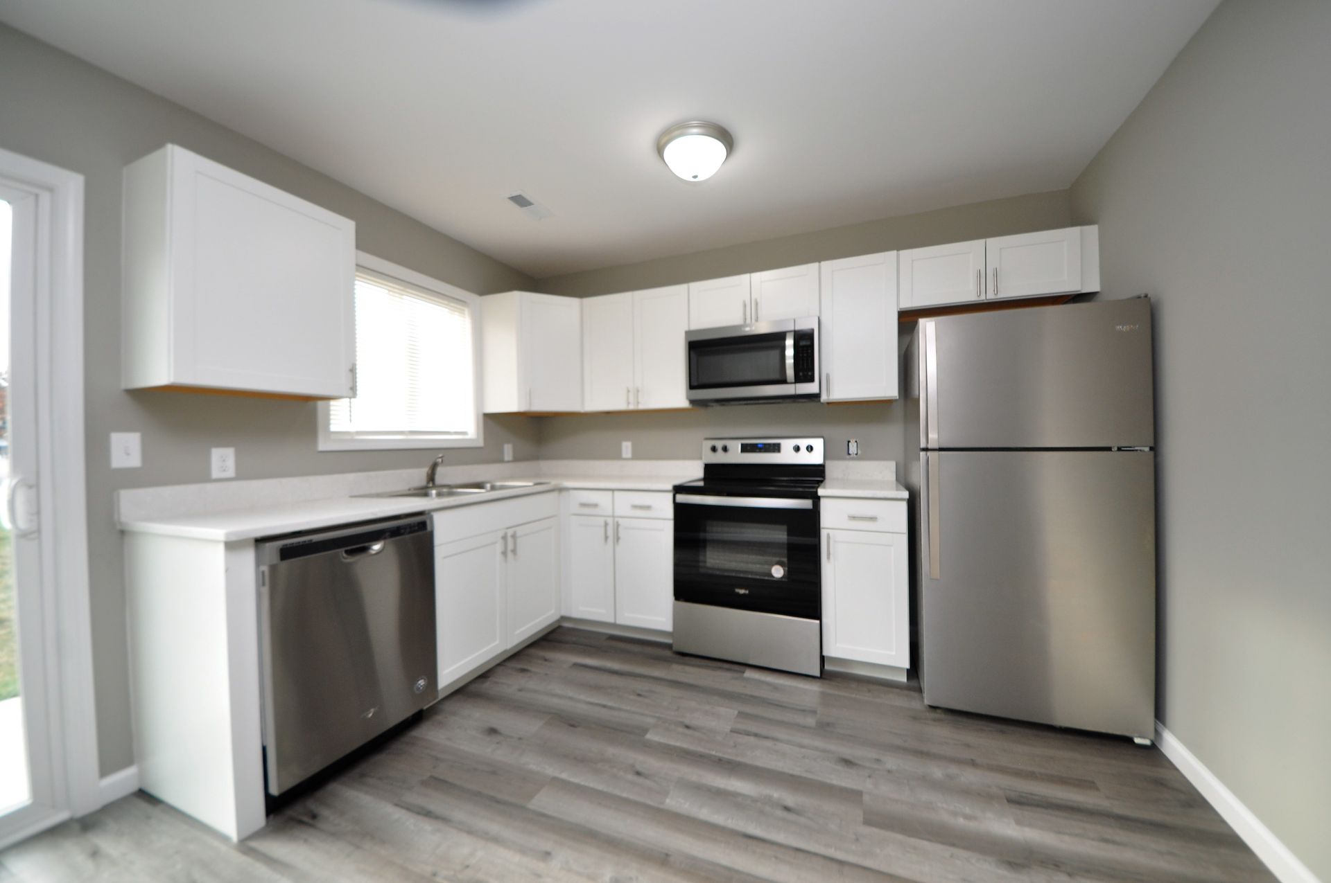 Bright modern kitchen with white cabinets, stainless appliances, and gray wood flooring