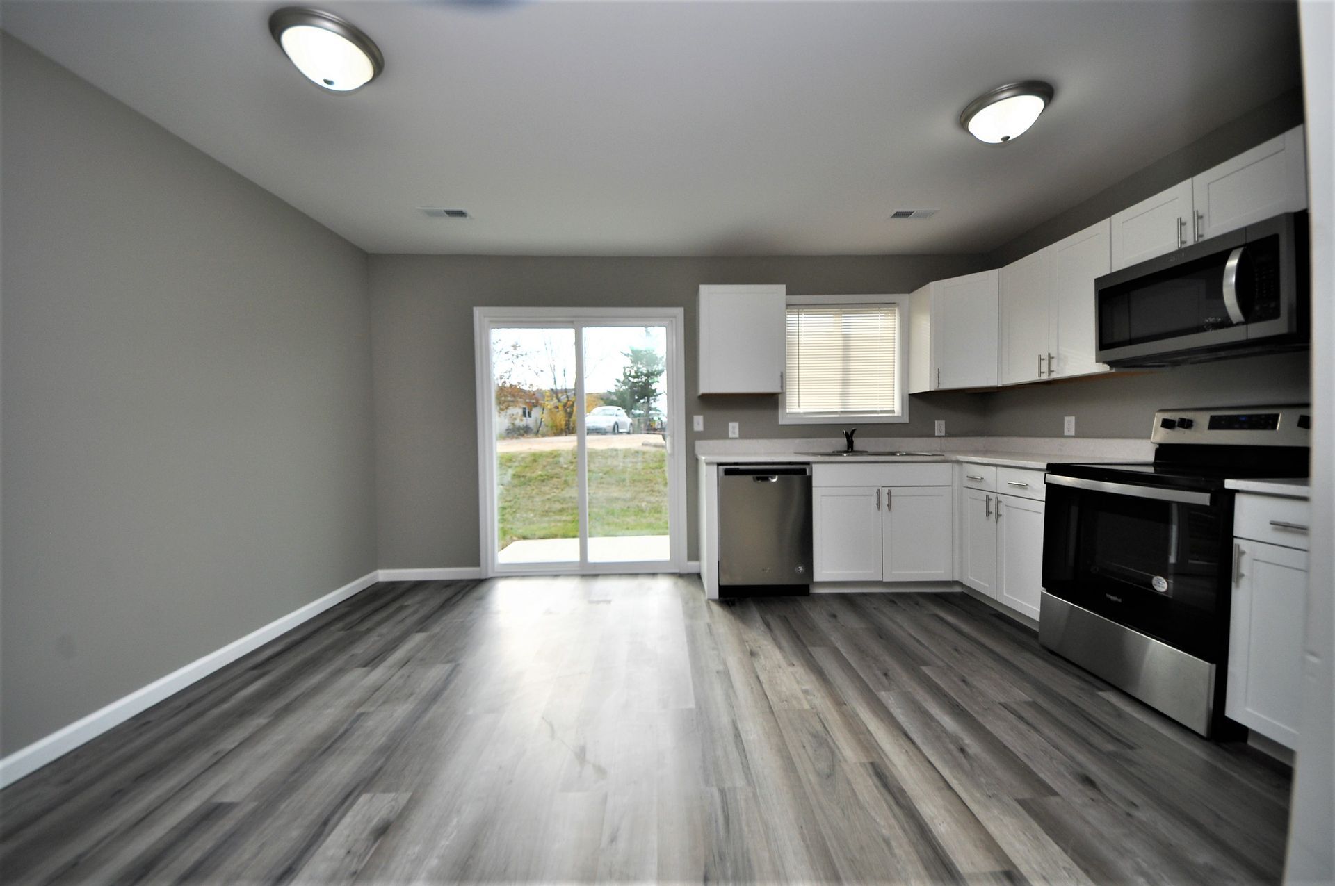 Modern kitchen and dining area with gray flooring, white cabinets, stainless appliances, and sliding glass door.