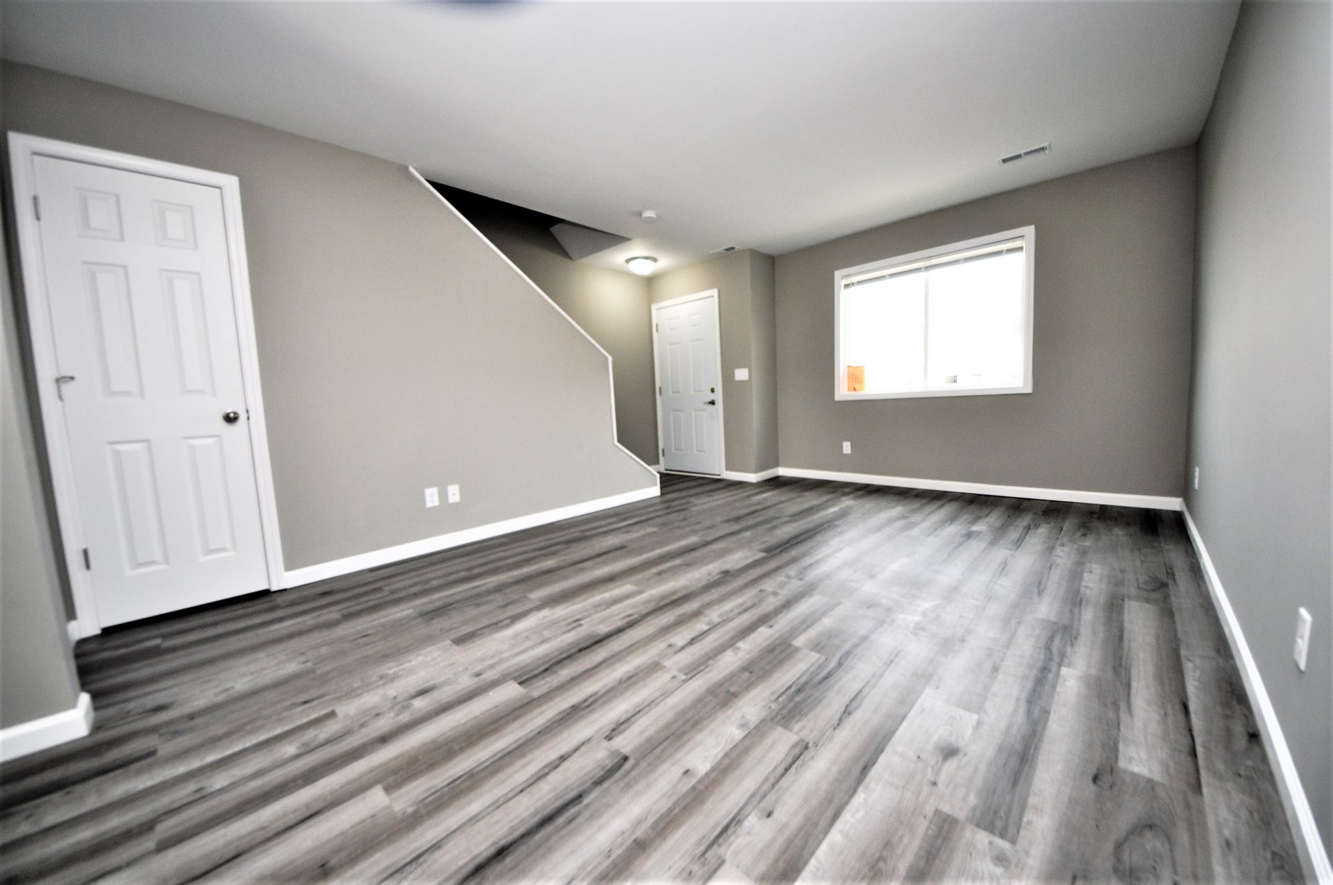 Empty gray living room with wood-look flooring, white closet doors, and a window letting in light