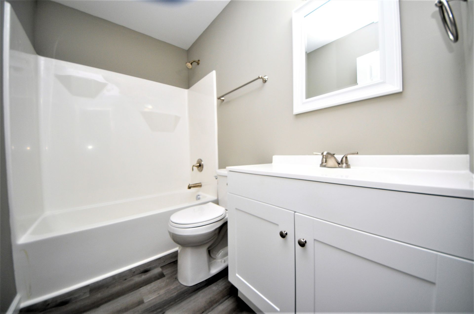 Small white bathroom with bathtub, toilet, vanity, and wall mirror on gray floor tiles