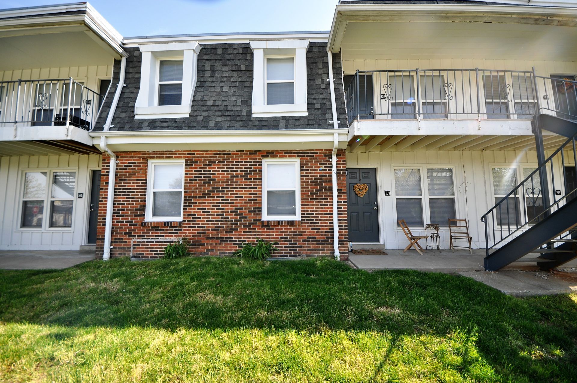 Apartment building facade with brick center, white siding, balconies, and green lawn in front