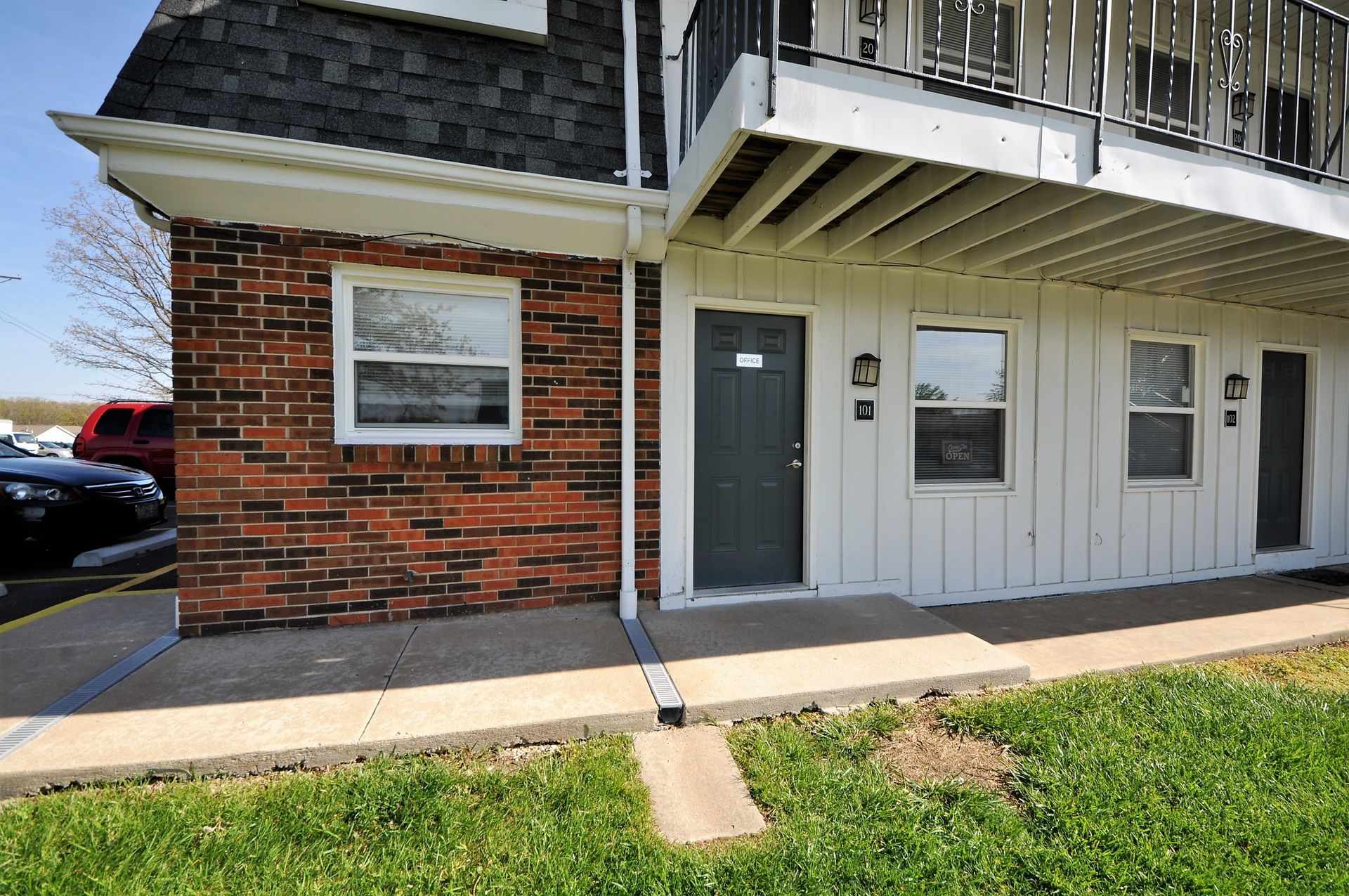 Apartment building entrance with brick and white siding, gray door, windows, and small grass lawn