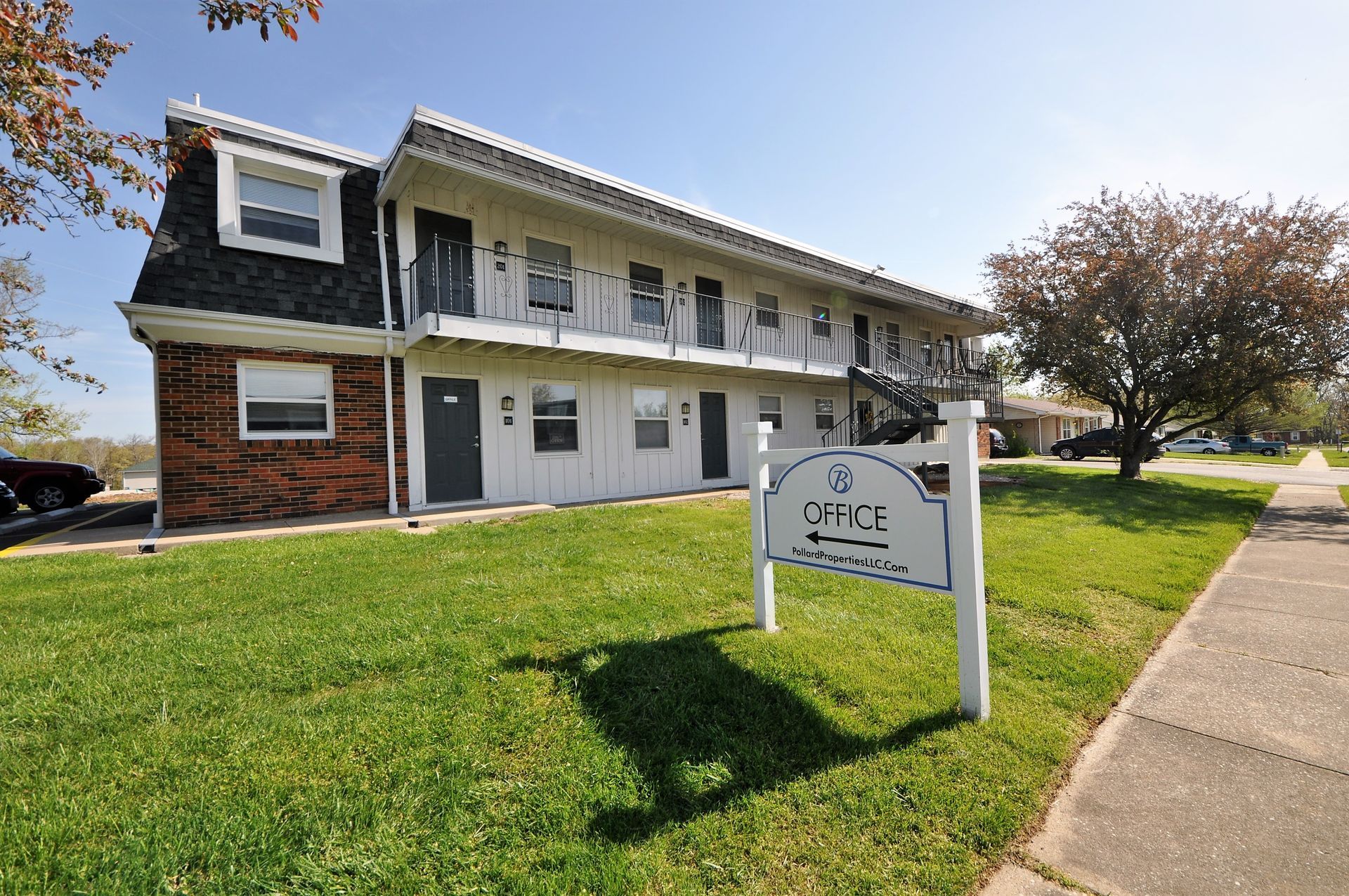 Two-story apartment building with a sign and sidewalk on a sunny day