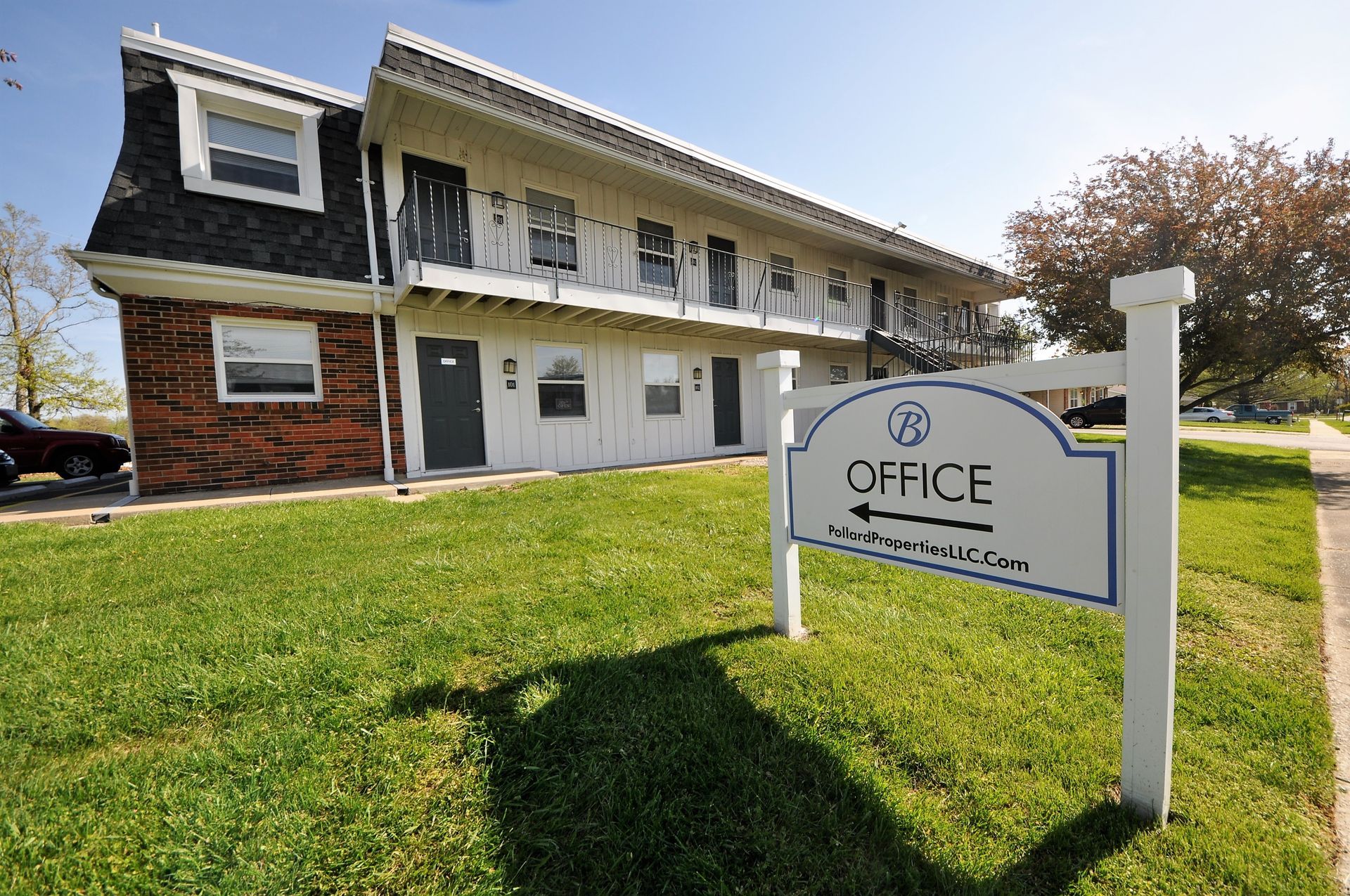 Office sign in front of a white two-story building with brick siding and a green lawn