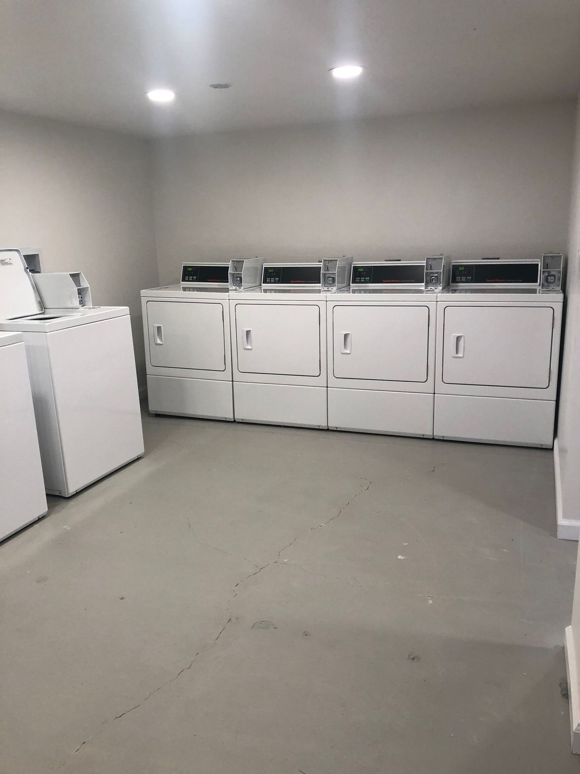 Laundry room with rows of white washers and dryers under recessed ceiling lights