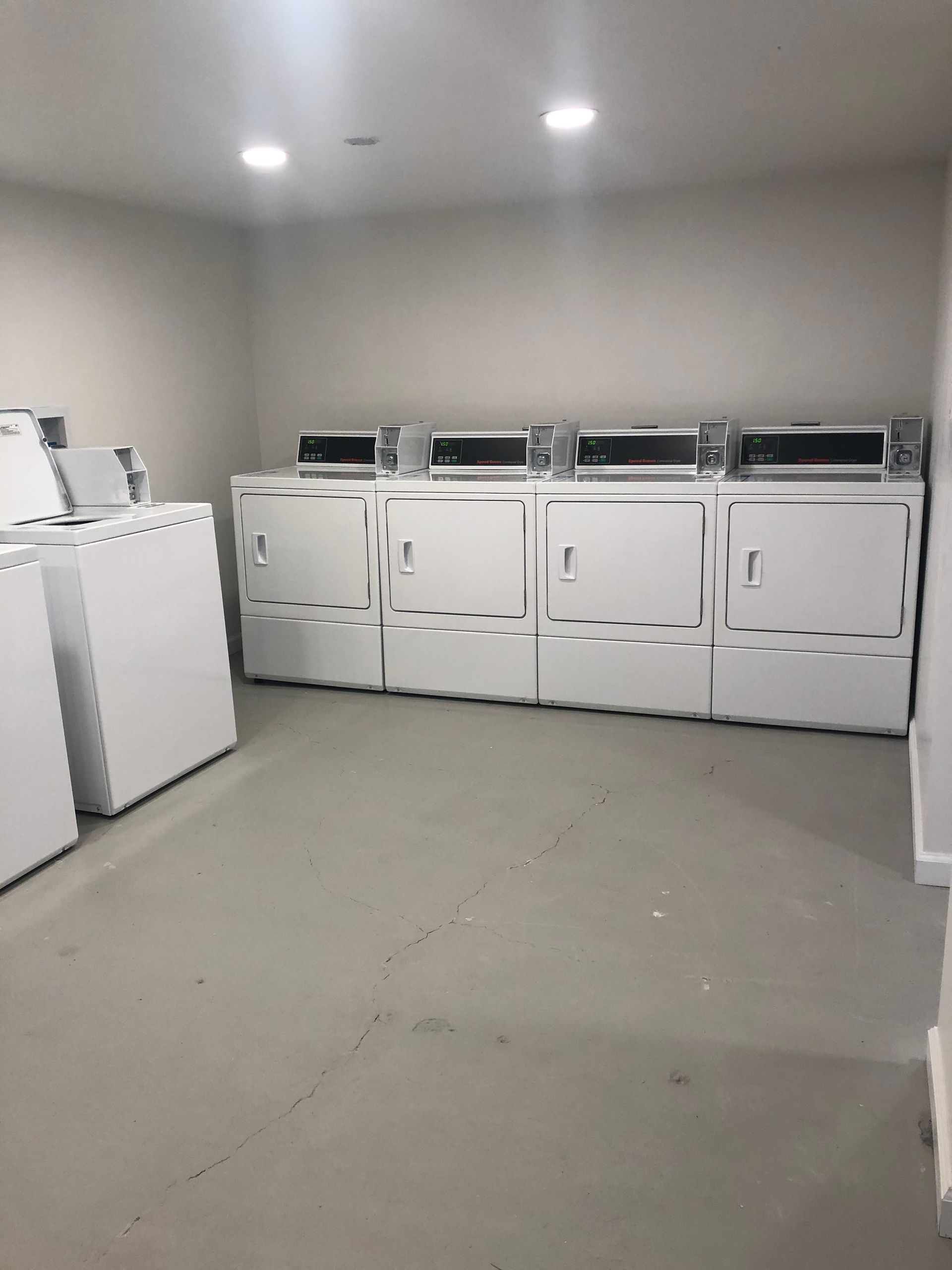 Laundry room with rows of white commercial washers and dryers under bright ceiling lights