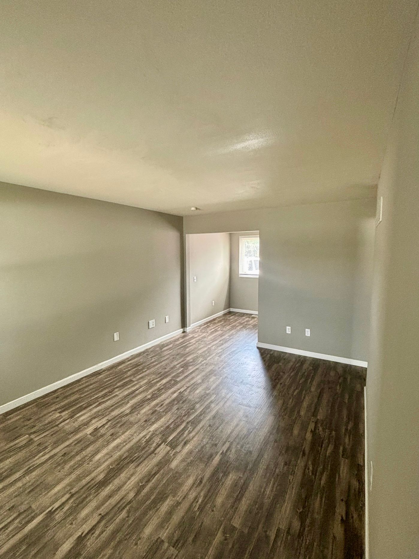 Empty living room with gray walls, dark wood floors, and a small window at the far end.