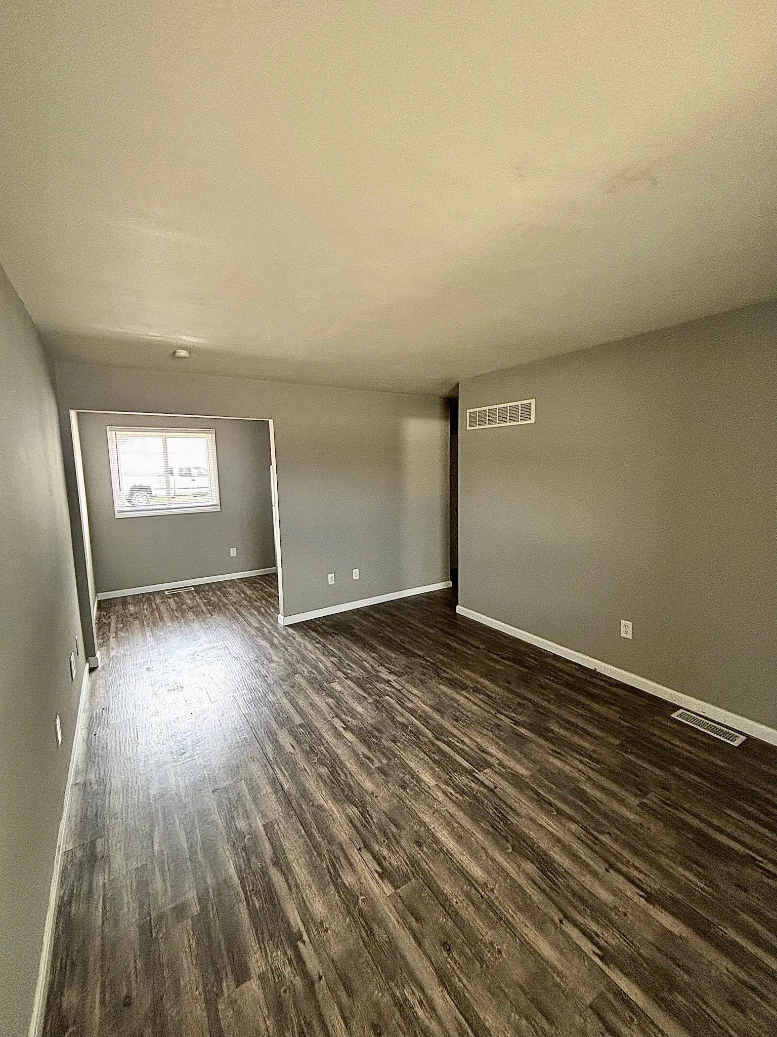 Empty unfurnished room with wood flooring, beige walls, and a windowed doorway to another space