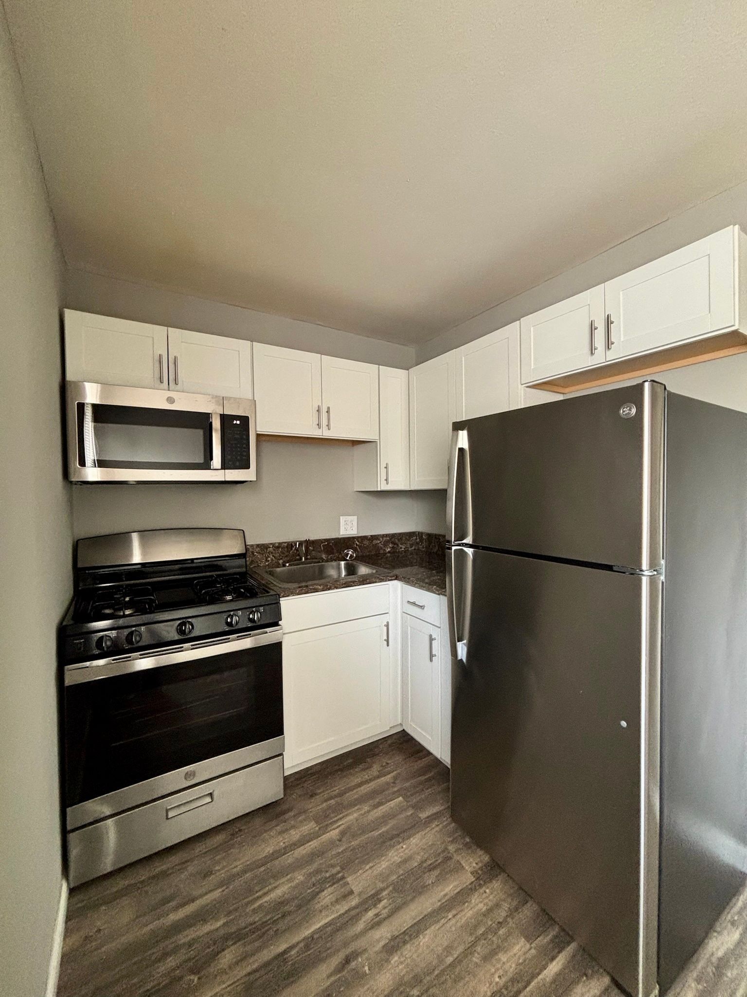 Small kitchen with white cabinets, stainless steel appliances, dark countertops, and wood-look flooring.