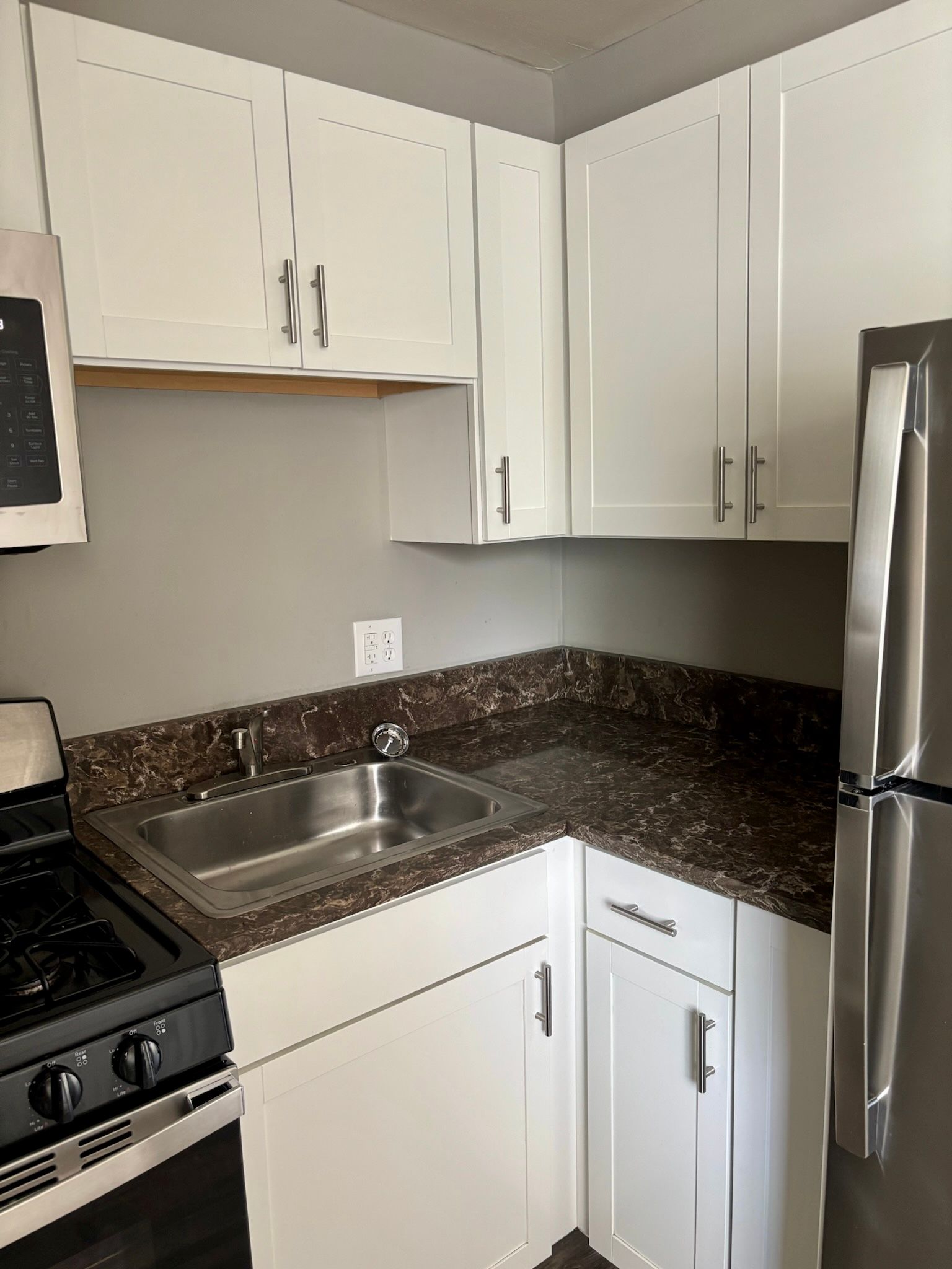 Compact kitchen with white cabinets, dark granite counters, stainless sink, stove, and refrigerator.