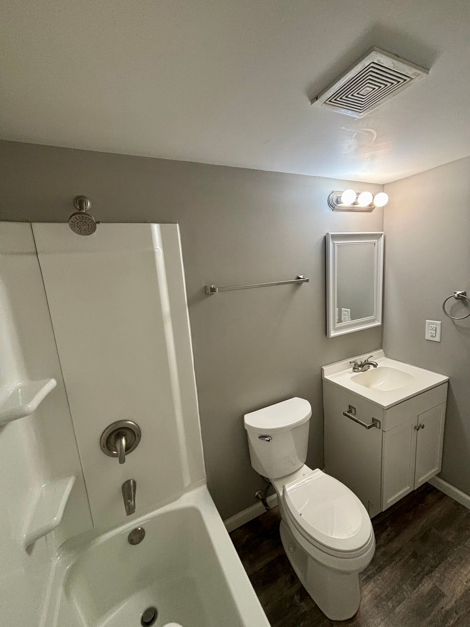 Small bathroom with a shower, toilet, vanity, mirror, and ceiling vent in neutral tones.