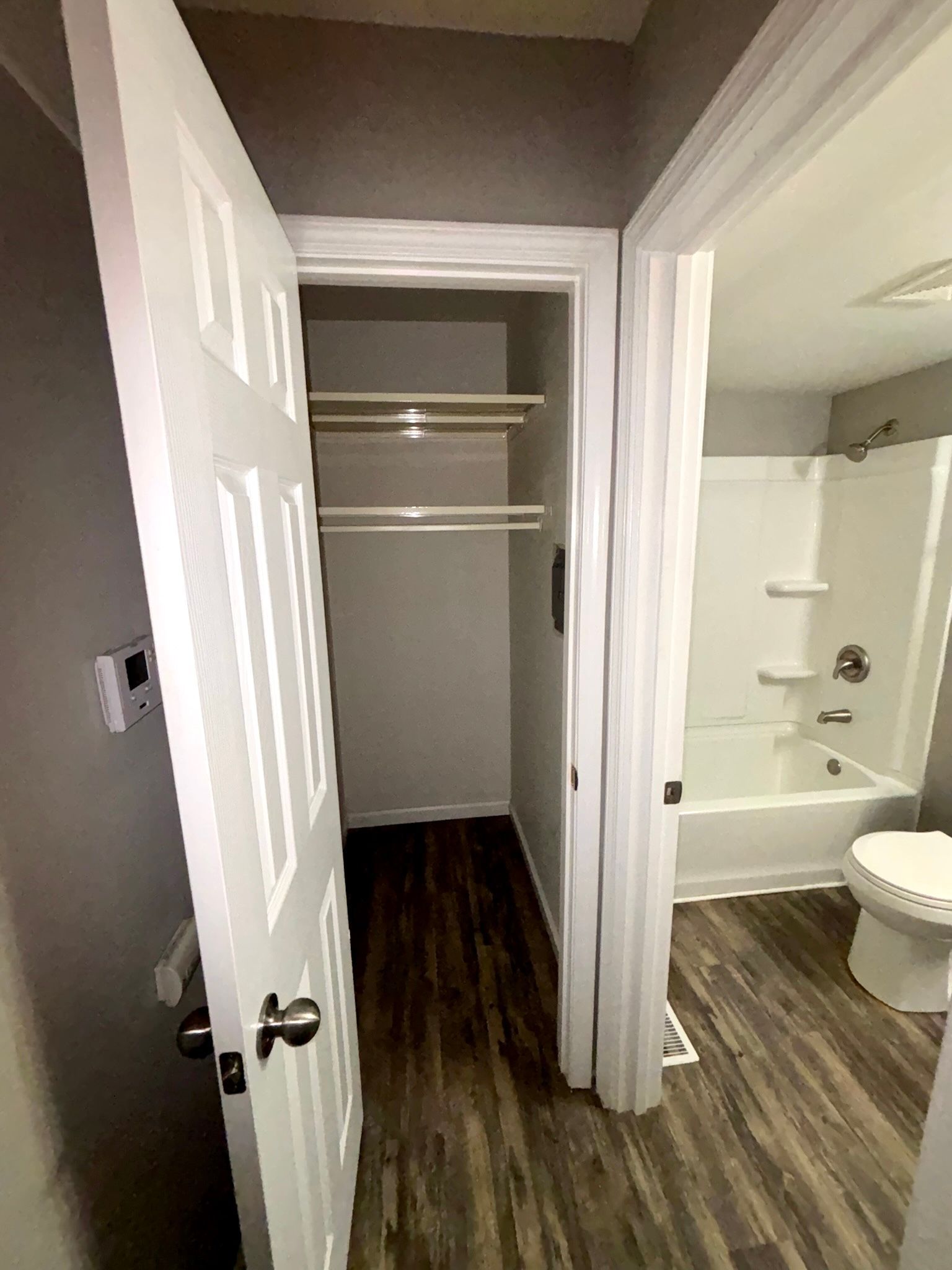 Empty closet beside a bathroom with wood-look flooring and a white tub/shower.