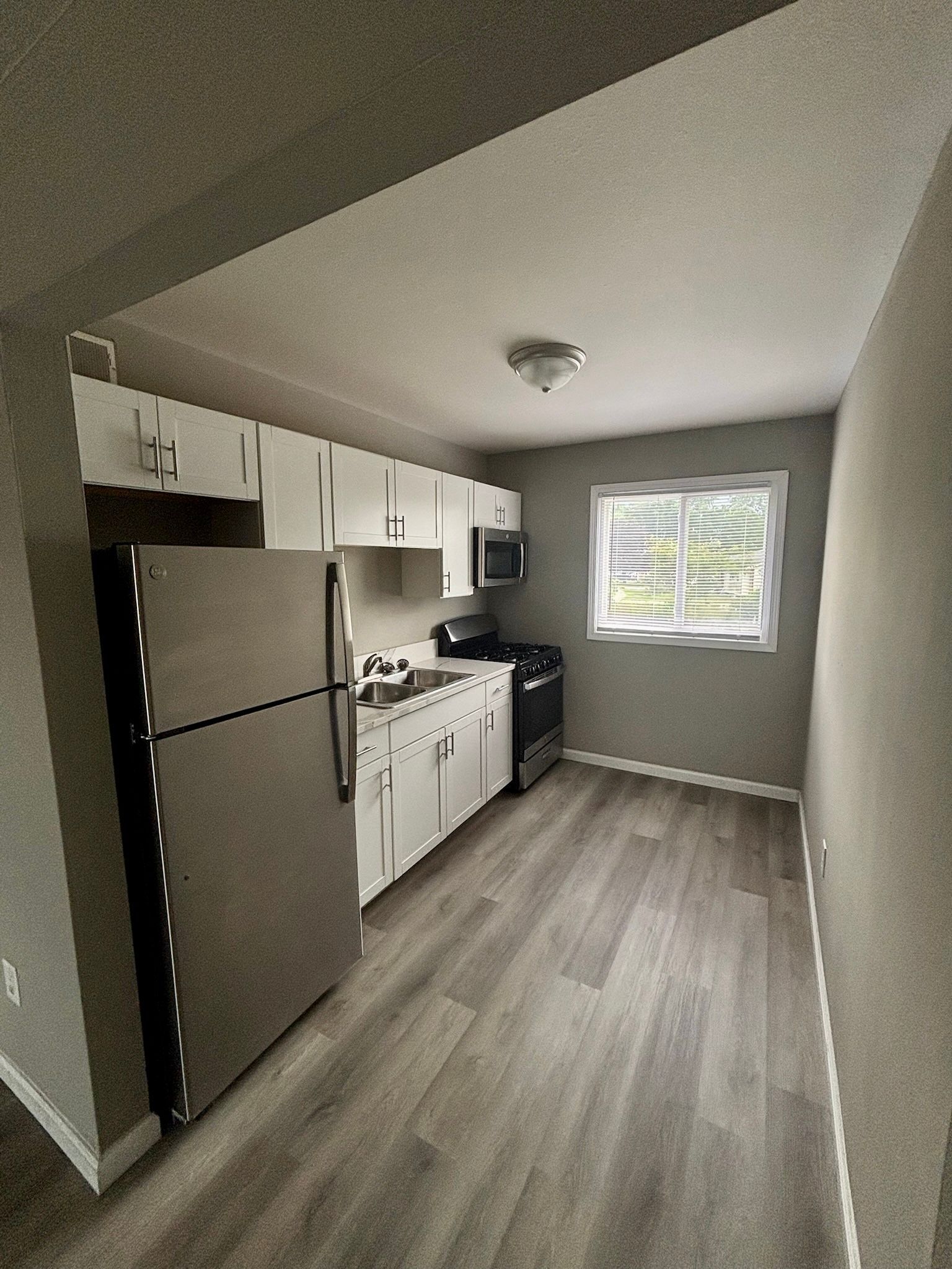 Small kitchen with stainless fridge, white cabinets, stove, and a window at the far end.