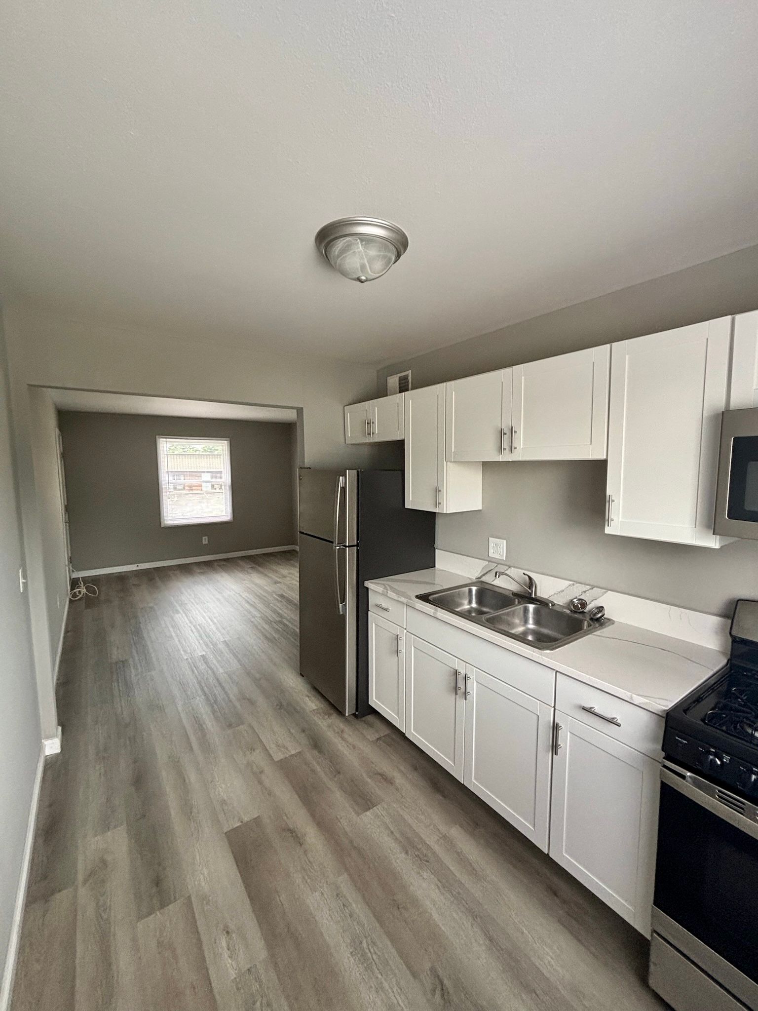 Empty modern kitchen with white cabinets, gray flooring, and stainless steel appliances.