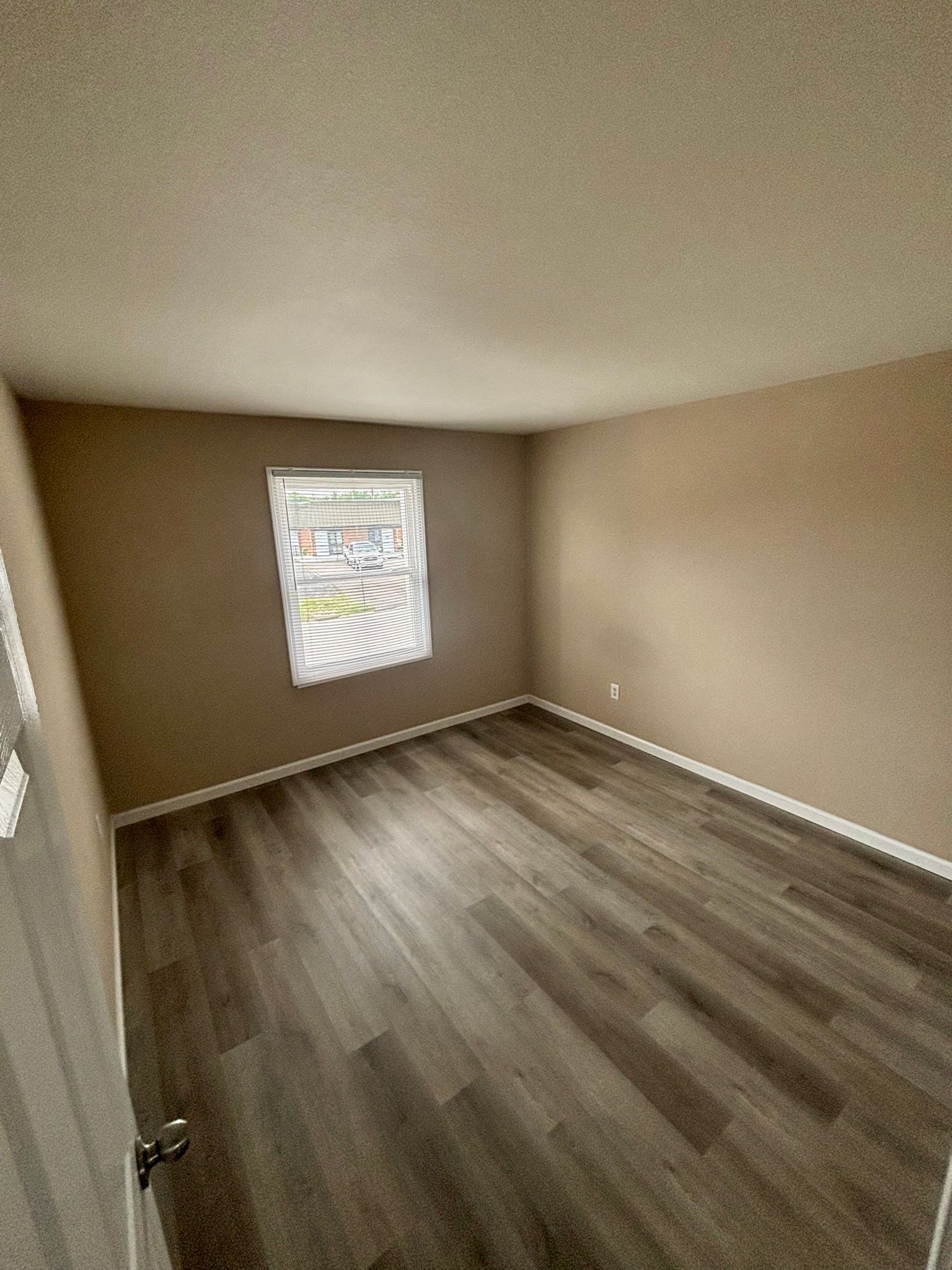 Empty beige room with wood-look flooring and a single window with blinds