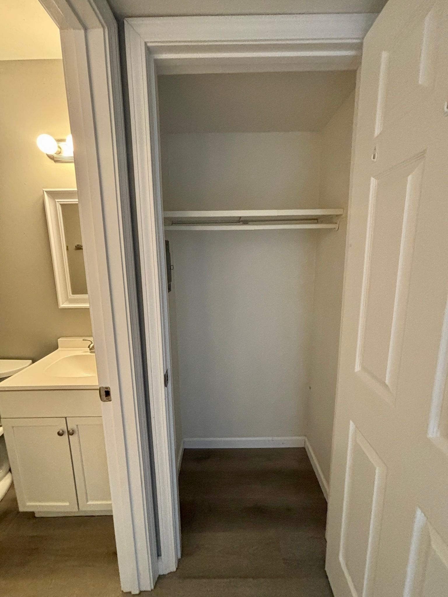 Empty bedroom closet with white bi-fold doors and a shelf, open in a gray room.
