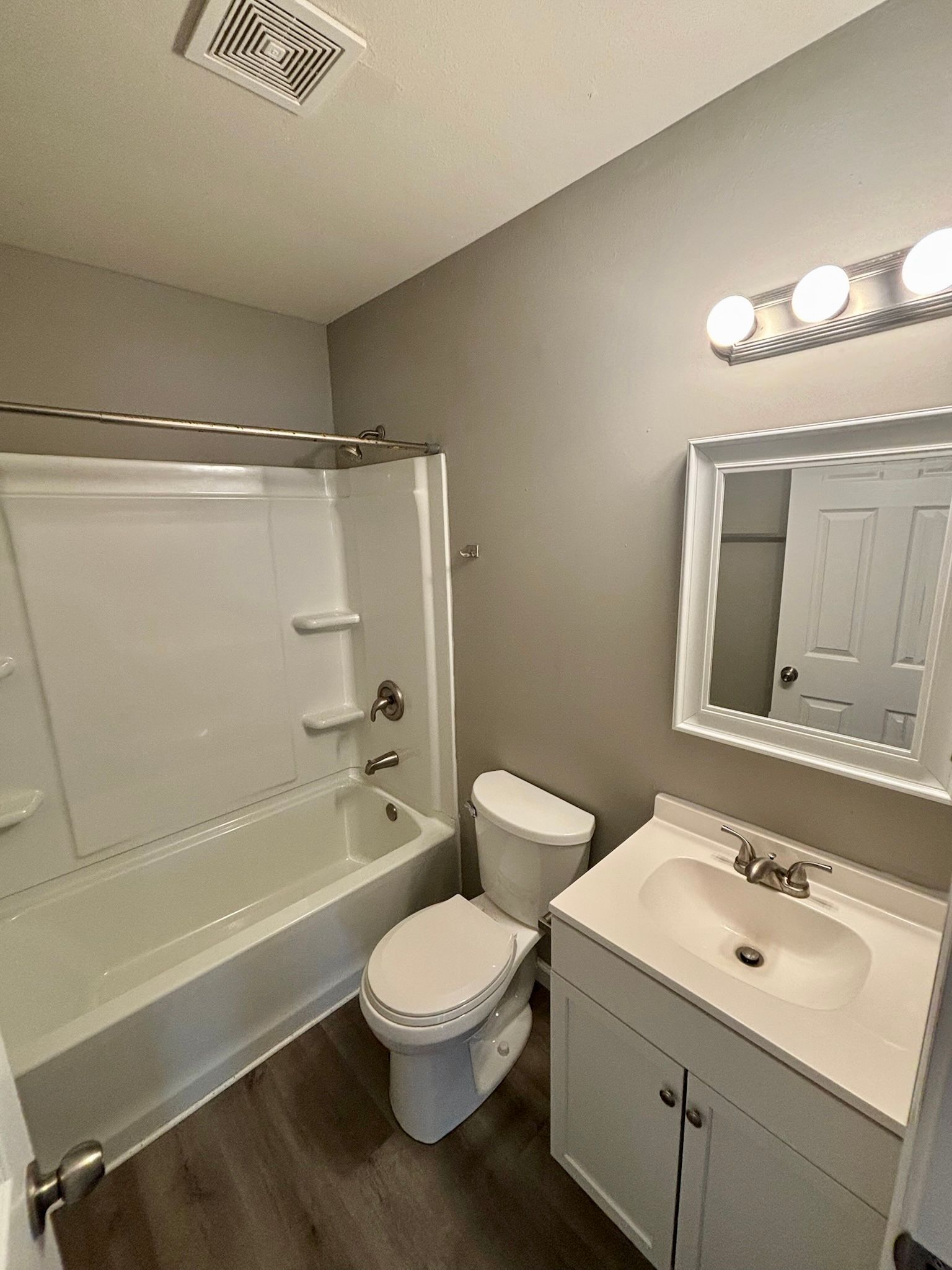 Small white bathroom with tub-shower, toilet, and vanity sink beneath a mirror.
