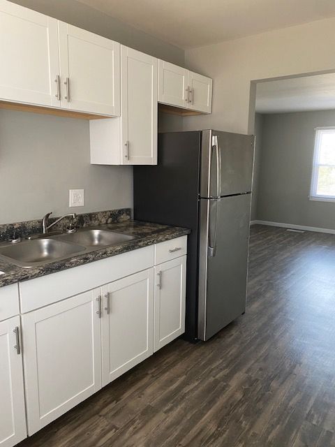 Small kitchen with white cabinets, gray countertop, stainless fridge, and wood-look flooring.