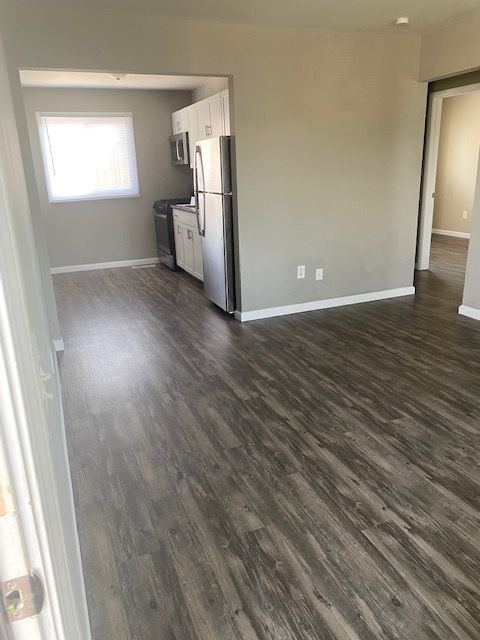 Empty apartment living area with gray wood floors and a small kitchen nook