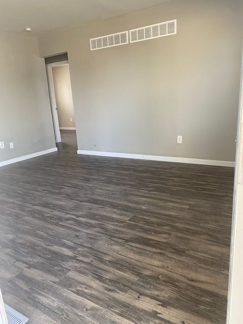 Empty room with gray walls, dark wood flooring, and a doorway near a wall vent.