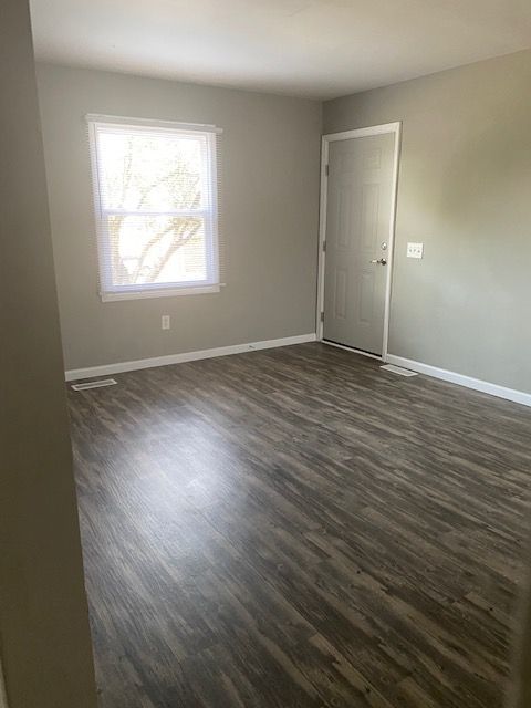 Empty room with gray walls, wood-look flooring, a window, and a closed white door.
