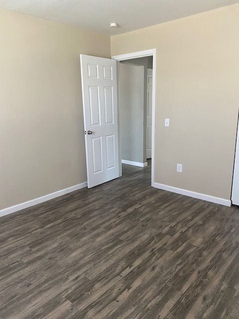 Empty beige room with wood-look flooring and an open white door leading to a hallway.