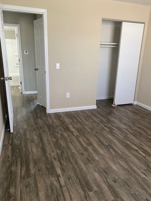 Empty bedroom with gray wood floors, beige walls, open door, and closet