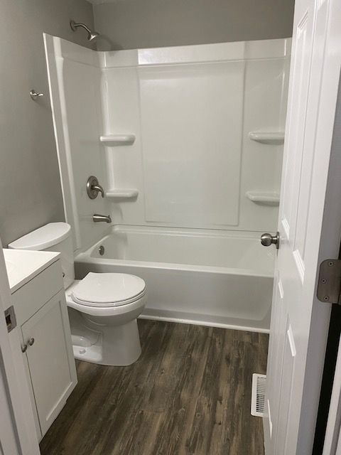 Accessible bathroom with white tub, toilet, sink vanity, and wood-look flooring