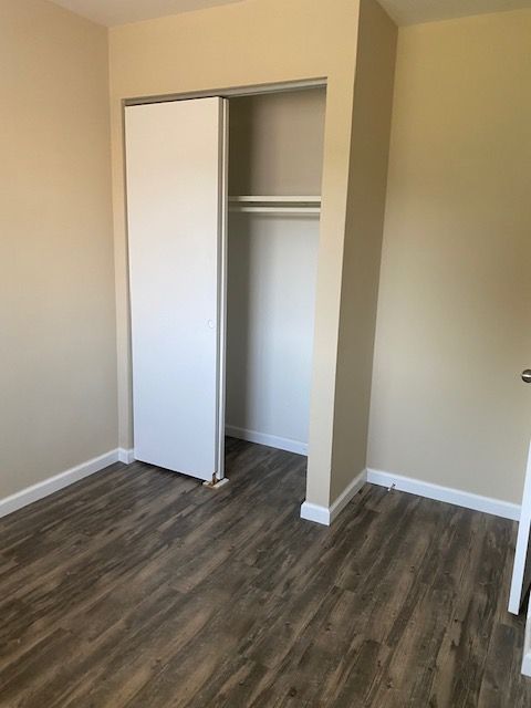 Empty beige bedroom with wood-look flooring and an open closet door