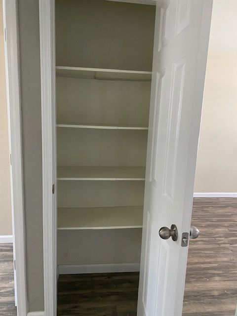Open closet with white shelves and doors in a room with wood flooring.