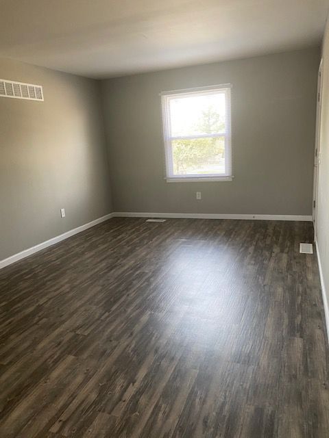 Empty room with gray walls, dark wood-look flooring, and a single window.