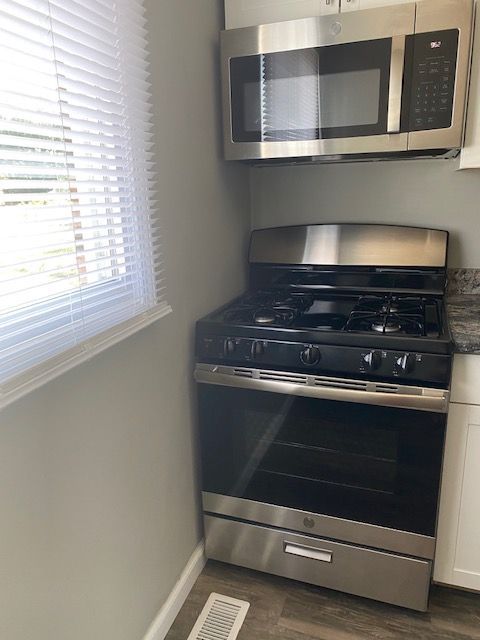 Small kitchen with stainless steel stove and microwave beside a window with blinds.
