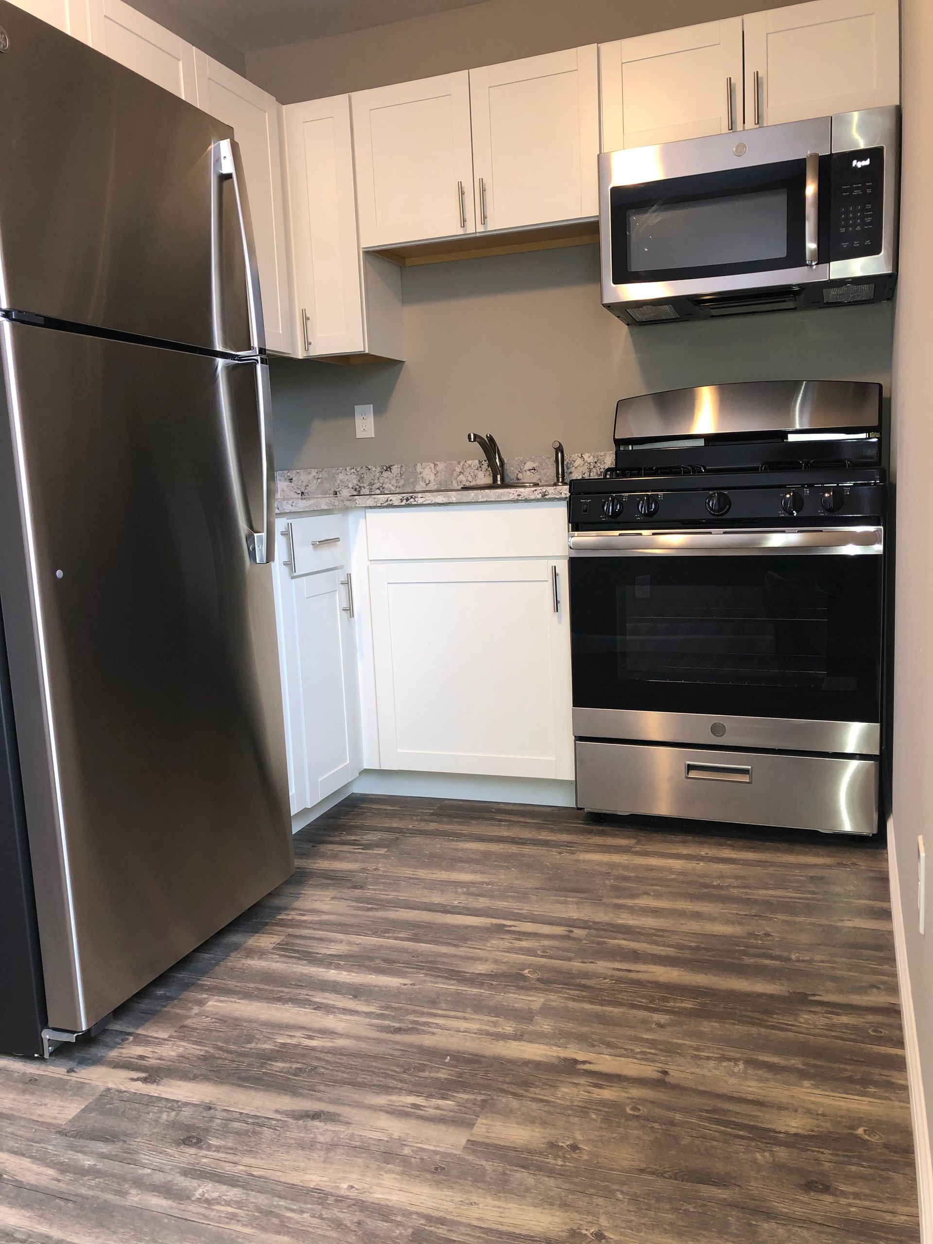 Small modern kitchen with stainless steel fridge, white dishwasher, black stove, microwave, and wood flooring