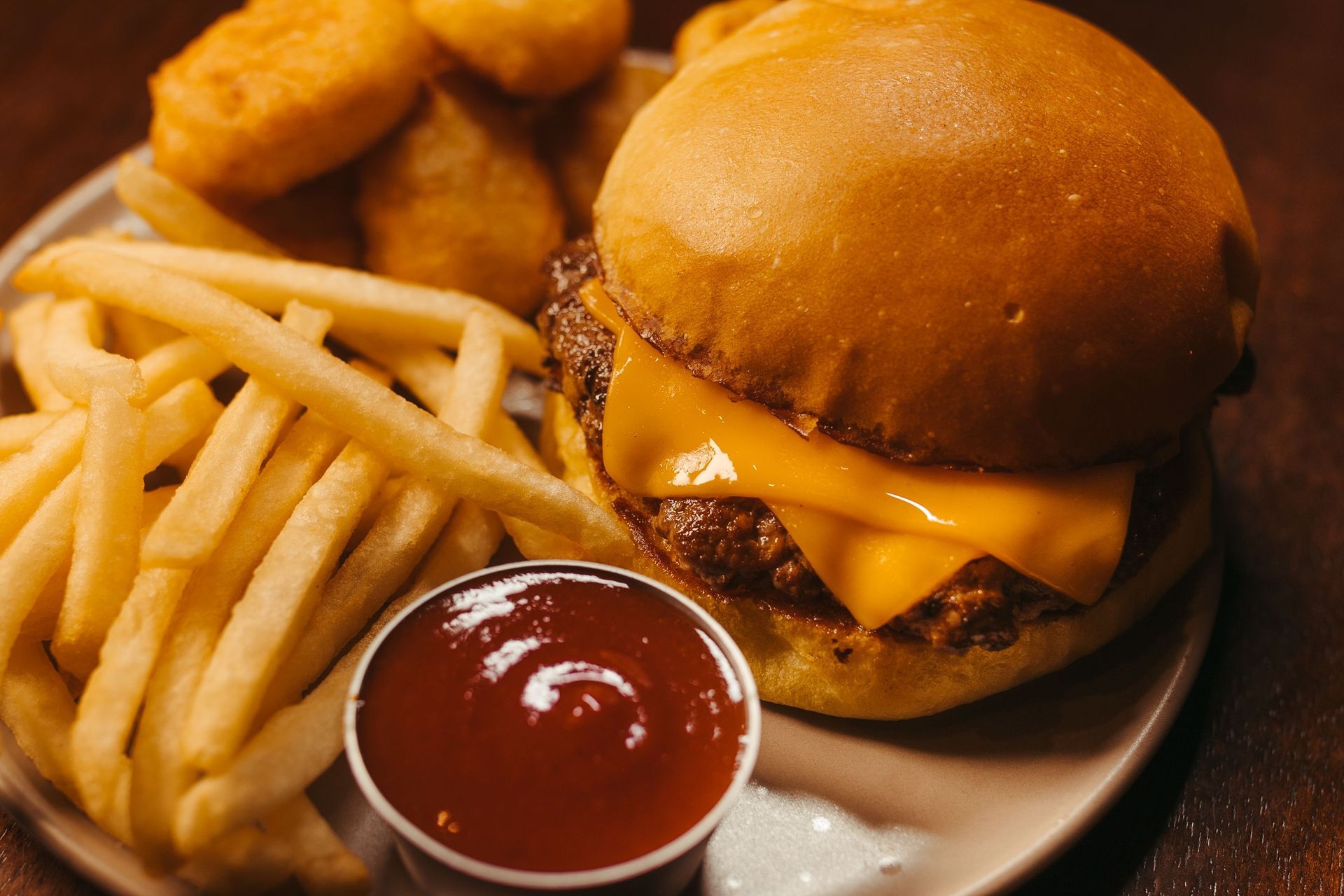 A hamburger and french fries on a white plate with a bud light bottle in the background
