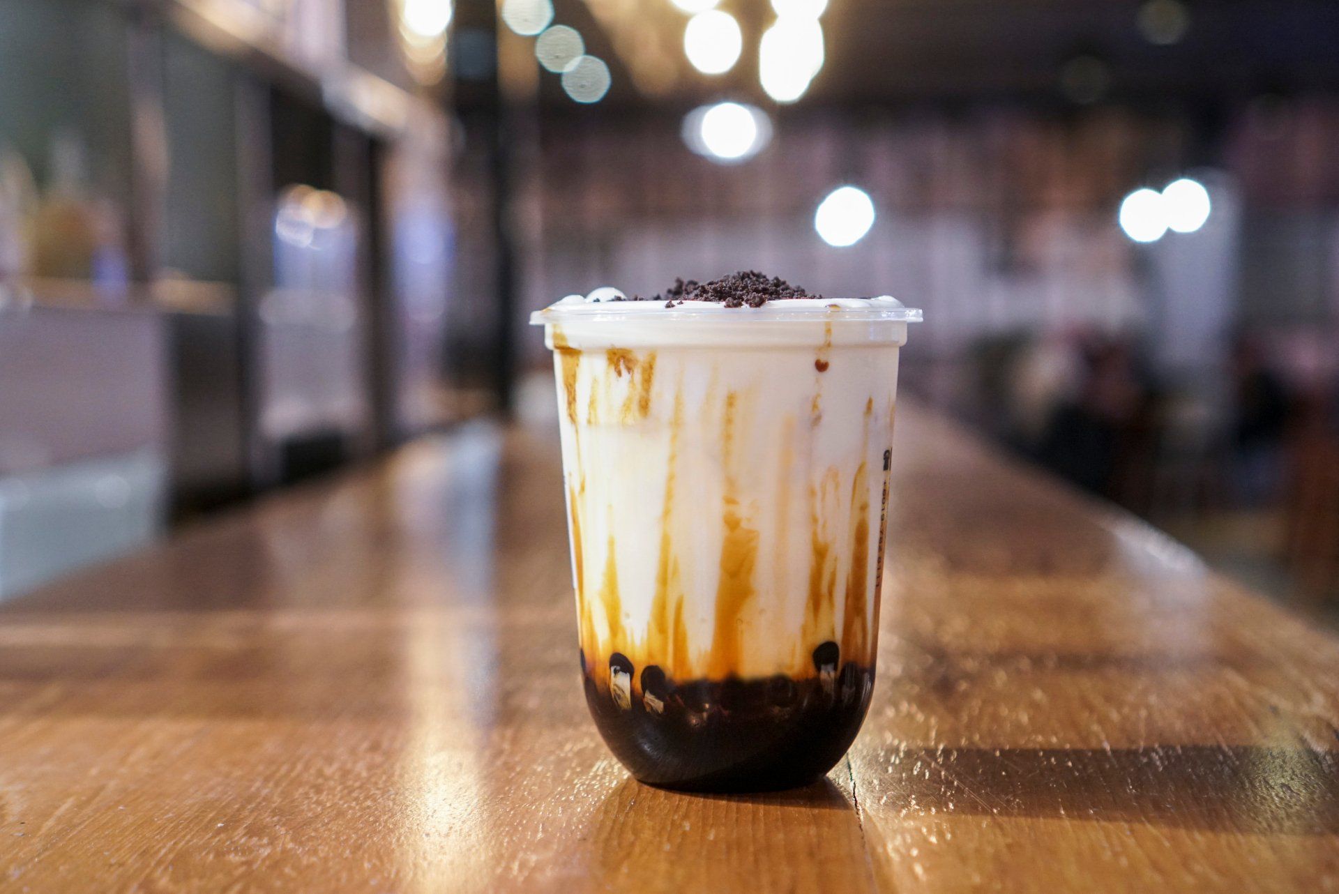 Brown sugar bubble drink. A plastic cup of fresh milk and brown sugar boba/bubble toppings and topped with chocolate cookies on wooden table.