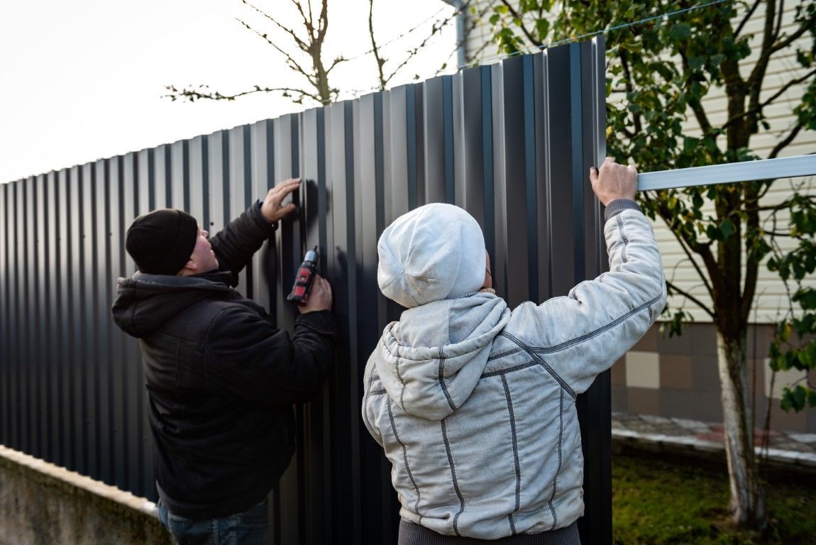 Two people installing a corrugated metal fence outdoors