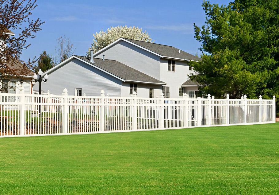 White suburban house with a white fence beside a green lawn under a blue sky