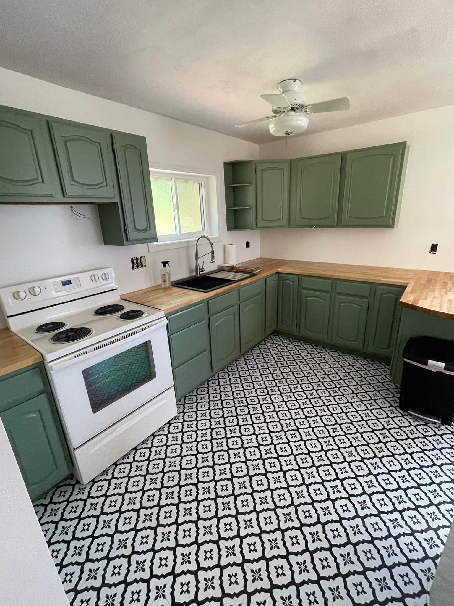 Green-painted kitchen with white appliances, wood countertops, and patterned black and white floor tiles.