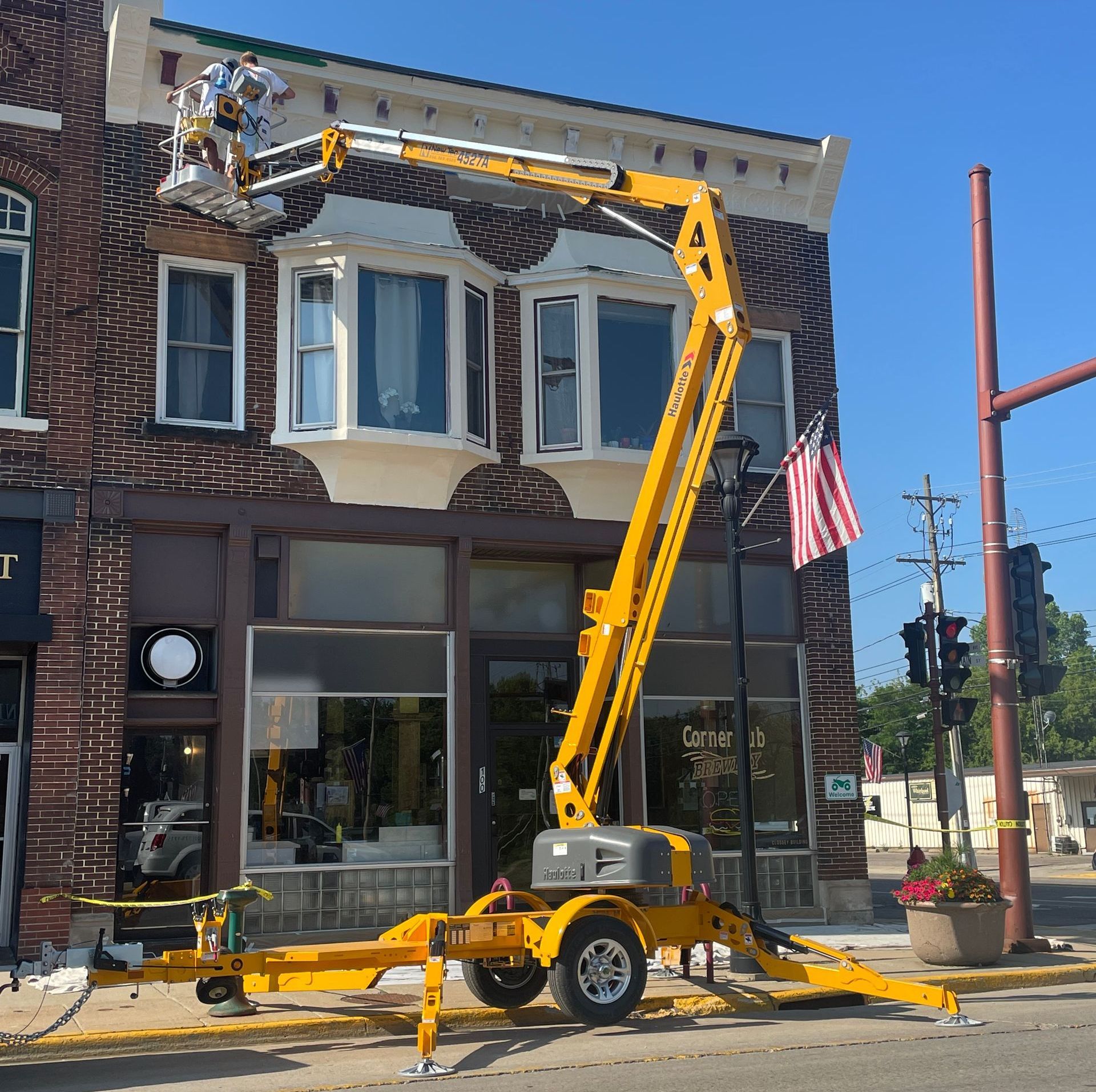 A yellow aerial lift is parked in front of a brick building