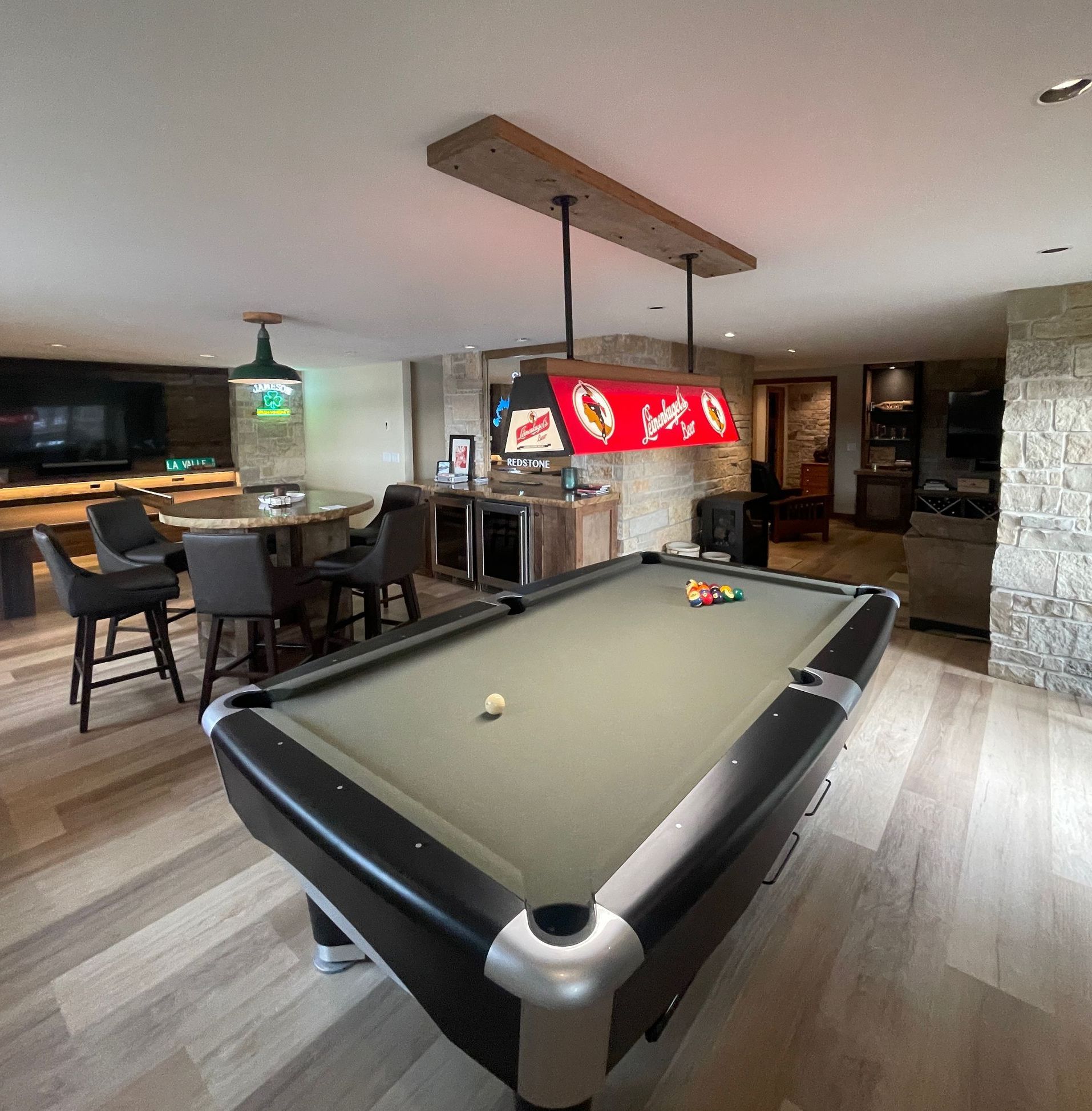 Pool table in a basement with bar seating, a tv, and a bar sign, all with wooden accents.