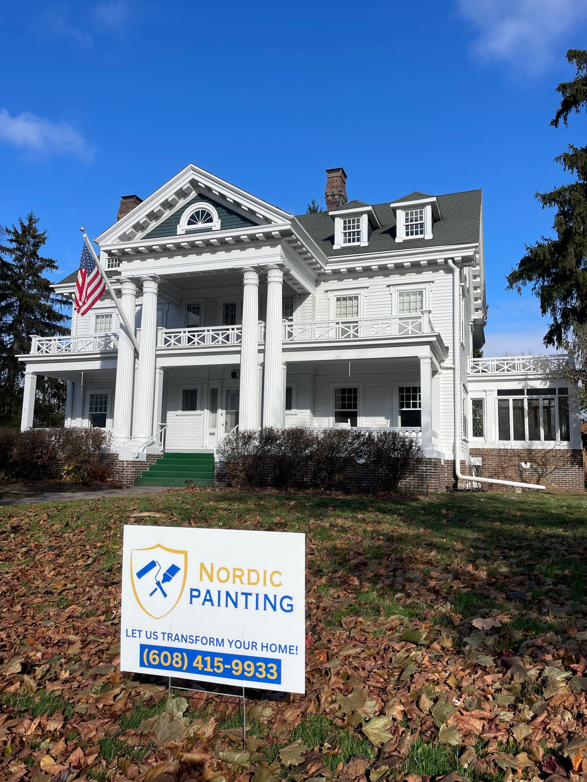 Nordic Painting sign in front of a white house with columns, American flag, and clear blue sky.
